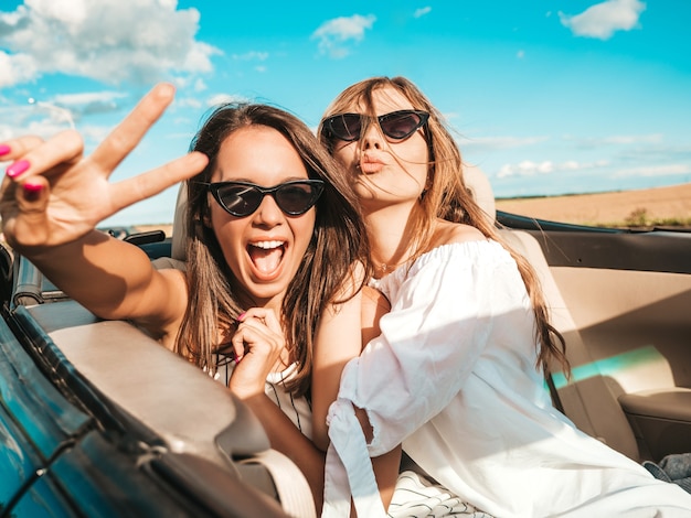 Ritratto di due giovani belle e sorridenti donne hipster in auto decappottabile