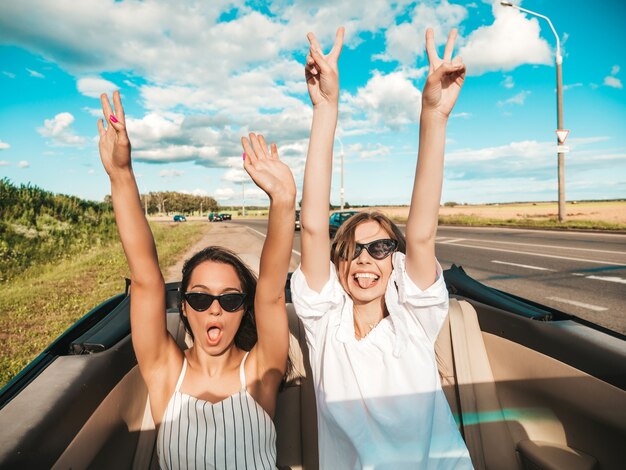 Ritratto di due giovani belle e sorridenti donne hipster in auto decappottabile