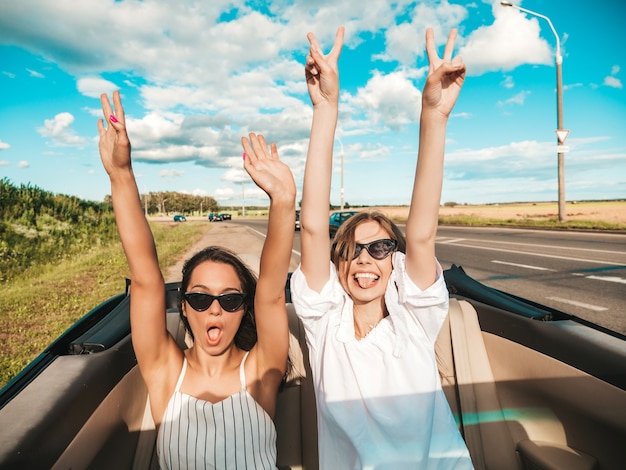 Ritratto di due giovani belle e sorridenti donne hipster in auto decappottabile