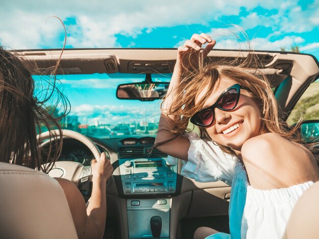 Ritratto di due giovani belle e sorridenti donne hipster in auto decappottabile