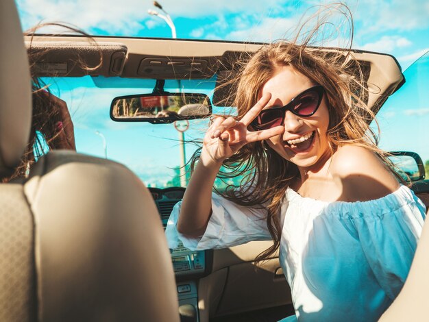 Ritratto di due giovani belle e sorridenti donne hipster in auto decappottabile