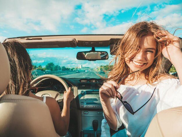 Ritratto di due giovani belle e sorridenti donne hipster in auto decappottabile