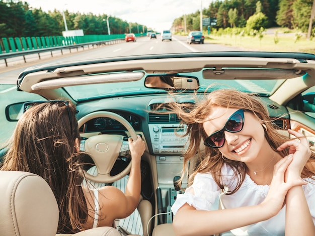 Ritratto di due giovani belle e sorridenti donne hipster in auto decappottabile