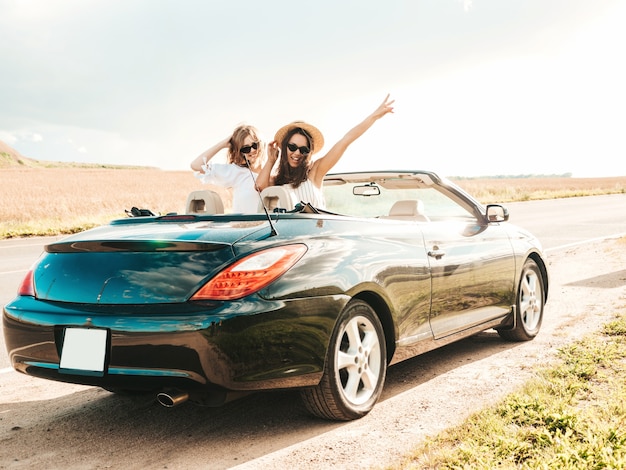 Ritratto di due giovani belle e sorridenti ragazze hipster in auto decappottabile