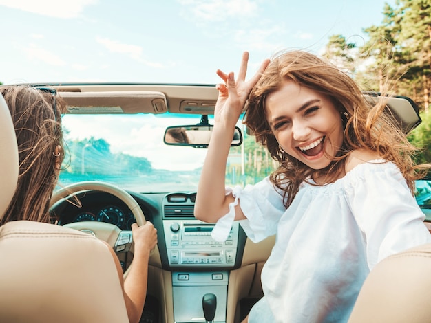 Ritratto di due giovani belle e sorridenti ragazze hipster in auto decappottabile