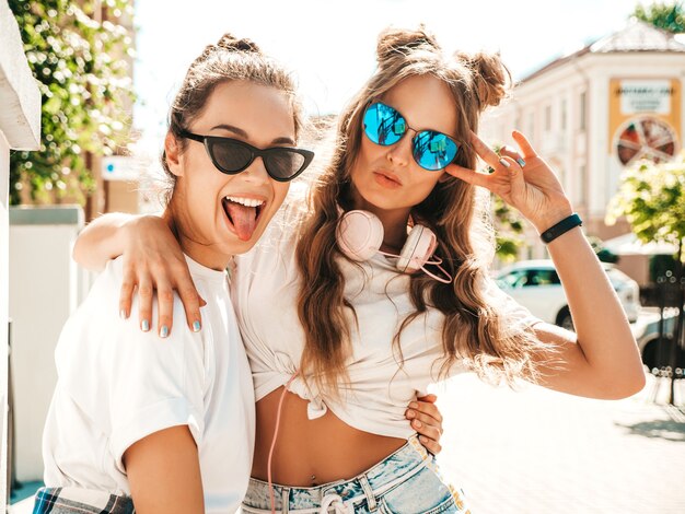 Ritratto di due giovani e belle donne hipster sorridenti in vestiti di t-shirt bianca estiva alla moda