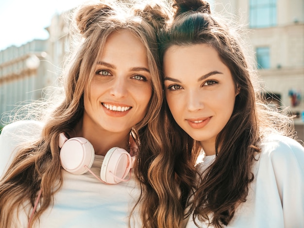 Ritratto di due giovani e belle donne hipster sorridenti in vestiti di t-shirt bianca estiva alla moda