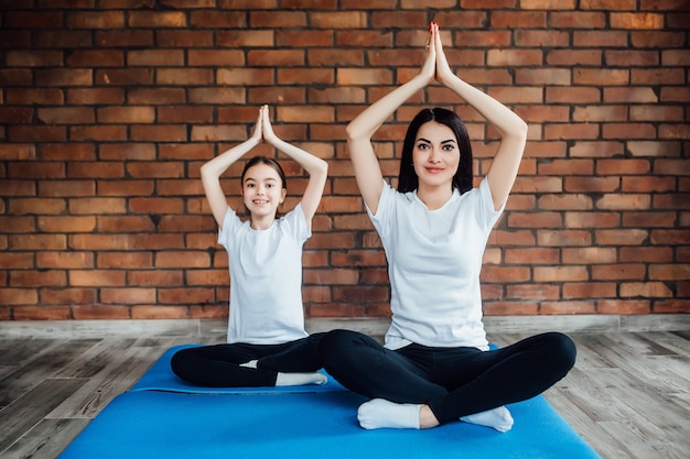 Ritratto di due ragazze attraenti che lavorano a casa, facendo esercizi di yoga sul tappetino blu, seduti in Easy, sul tappetino blu.