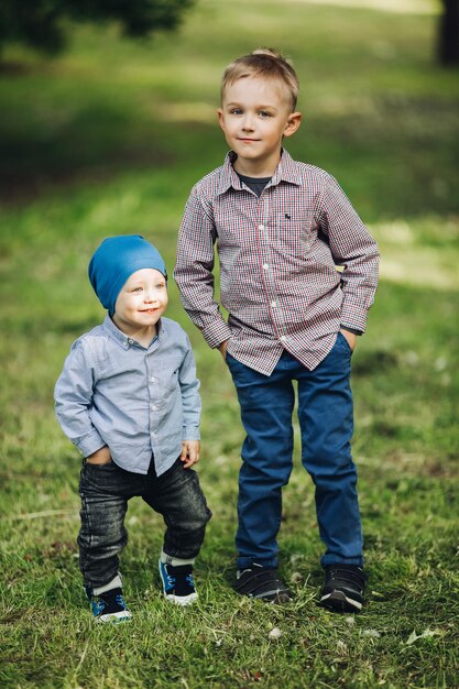 Ritratto di due ragazzini che indossano un look casual in posa nel parco tenendosi per mano nelle tasche Belli fratelli che camminano e giocano insieme Concetto di abbigliamento per bambini alla moda ed elegante