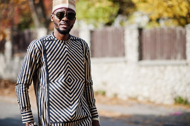 Ritratto di elegante uomo afroamericano nero con cappello e occhiali da sole su sfondo autunnale soleggiato Persone ricche in africa in abito tradizionale