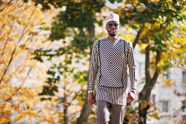 Ritratto di elegante uomo afroamericano nero con cappello e occhiali da sole su sfondo autunnale soleggiato