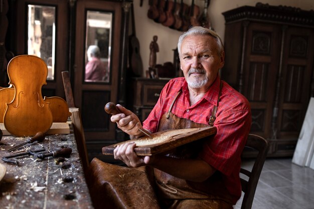 Ritratto di falegname senior che tiene strumenti e legno nella sua bottega antiquata