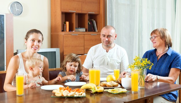 Ritratto di famiglia felice multigeneration mangiare fringuelli con succo di frutta a casa insieme