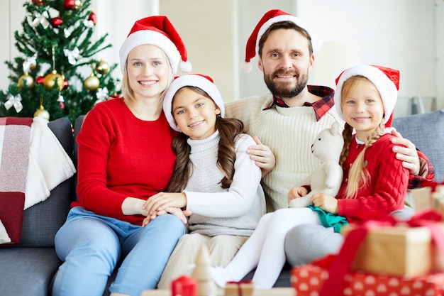 Ritratto di famiglia felice seduto sul divano con cappelli di Babbo Natale