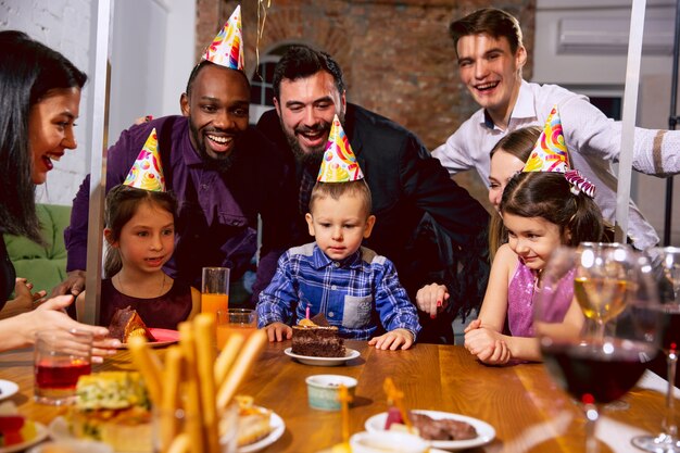 Ritratto di famiglia multietnica felice che celebra un compleanno a casa. Grande famiglia che mangia torta e beve vino mentre saluta e si diverte i bambini. Celebrazione, famiglia, festa, concetto di casa.