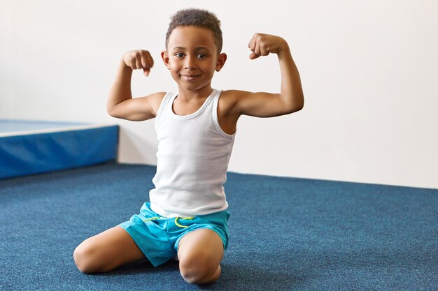 Ritratto di felice allegro ragazzo dalla pelle scura con breve acconciatura afro che si esercita al centro fitness