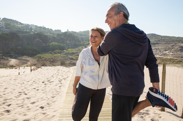 Ritratto di felice coppia senior facendo esercizi fisici. Donna e uomo sorridenti in piedi vicino all'aperto allungando le gambe cercando di mantenersi in forma e in salute. Sport, stile di vita sano del concetto di persone anziane