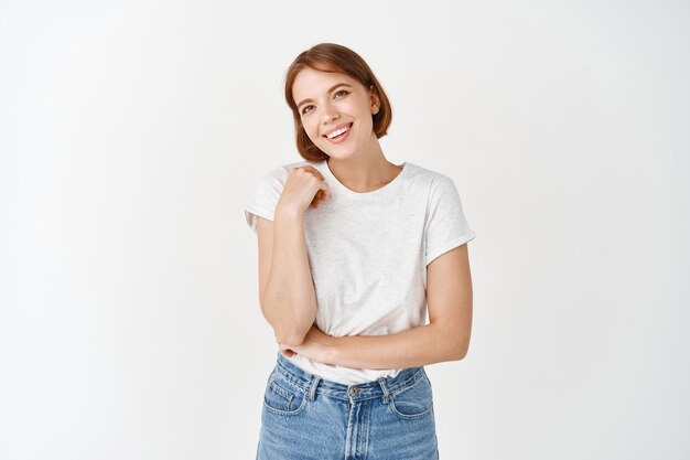 Ritratto di felice ragazza naturale, sorridente e ridente di gioia, dall'aspetto spensierato, in piedi in abiti casual contro il muro bianco