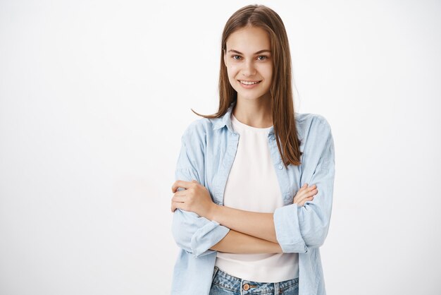 Ritratto di fiducioso di bell'aspetto audace donna in camicetta blu su t-shirt attraversando le mani sul petto e sorridendo felice e sicuro di sé