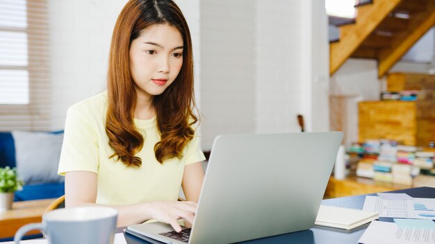 Ritratto di freelance Asia donne abbigliamento casual utilizzando laptop lavorando nel soggiorno di casa. Lavoro da casa, lavoro a distanza, autoisolamento, allontanamento sociale, quarantena per la prevenzione del coronavirus.