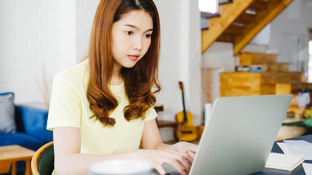 Ritratto di freelance Asia donne abbigliamento casual utilizzando laptop lavorando nel soggiorno di casa. Lavoro da casa, lavoro a distanza, autoisolamento, allontanamento sociale, quarantena per la prevenzione del coronavirus.