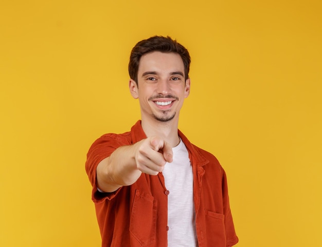 Ritratto di giovane allegro attraente che punta il dito contro la fotocamera e in piedi isolato su sfondo