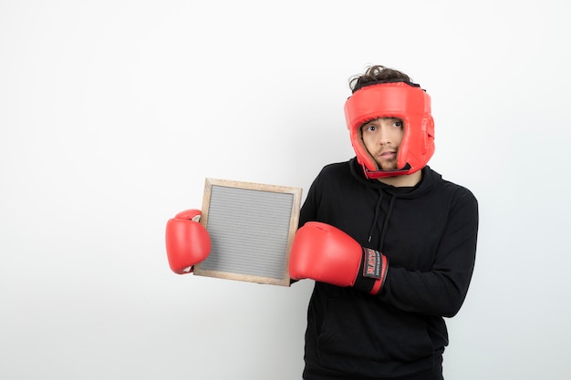 Ritratto di giovane atletico in cappello rosso di boxe che tiene cornice vuota.