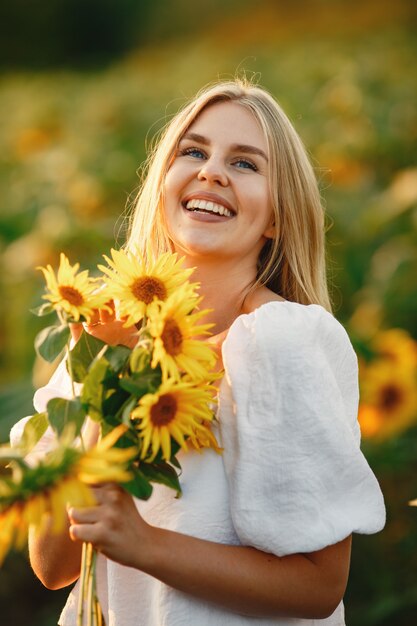 Ritratto di giovane bella donna bionda nel campo di girasoli in controluce. Concetto di campagna estiva Donna e girasoli. Luce estiva. Bellezza all'aperto.