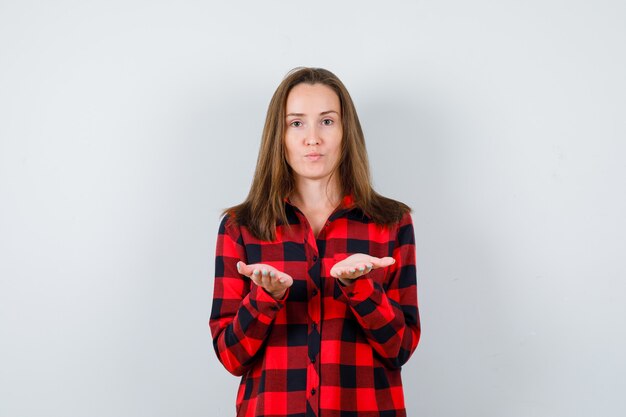 Ritratto di giovane bella donna che finge di tenere qualcosa in una camicia casual e sembra fiduciosa in vista frontale