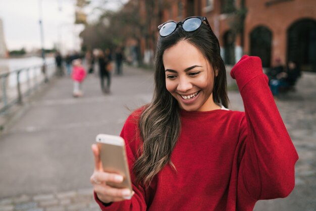 Ritratto di giovane bella donna che tiene il suo telefono cellulare con espressione di successo, celebrando qualcosa. Concetto di successo.