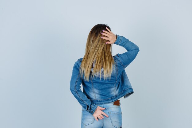 Ritratto di giovane bella donna che tiene le mani dietro la schiena e la testa in abito di jeans, vista posteriore