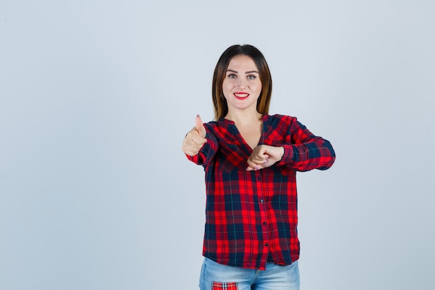 Ritratto di giovane bella donna con la mano davanti a se stessa, che mostra il pollice in una camicia casual e sembra allegra vista frontale