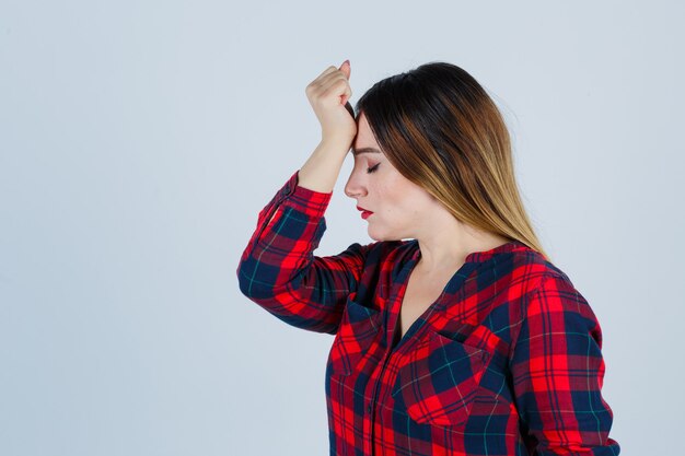 Ritratto di giovane bella donna con la mano sulla fronte in camicia casual e guardando la vista frontale pensierosa