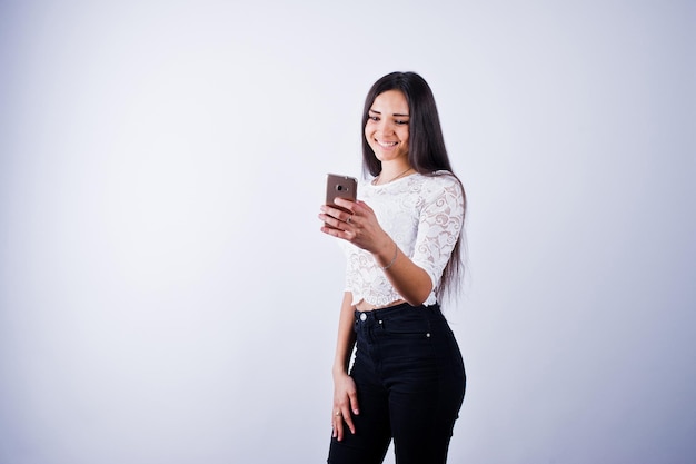 Ritratto di giovane bella donna in top bianco e pantaloni neri che usa il suo telefono