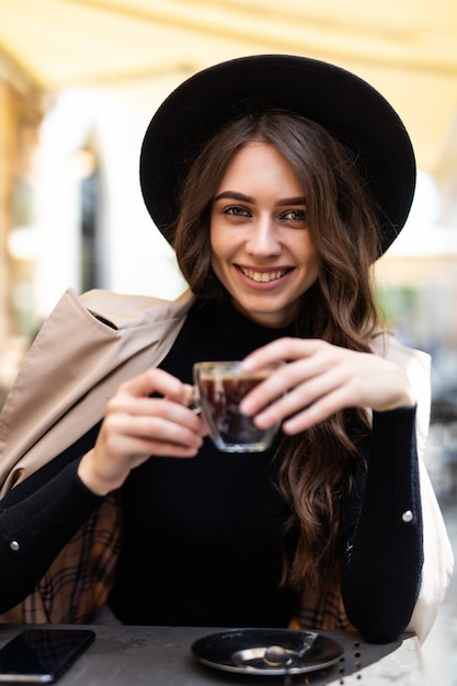 Ritratto di giovane bella donna seduta in un caffè all'aperto di bere caffè