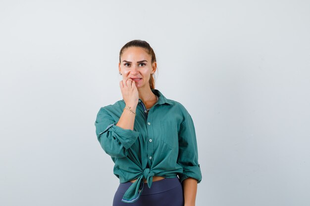 Ritratto di giovane bella femmina che controlla i suoi denti in camicia verde e che guarda esitante vista frontale