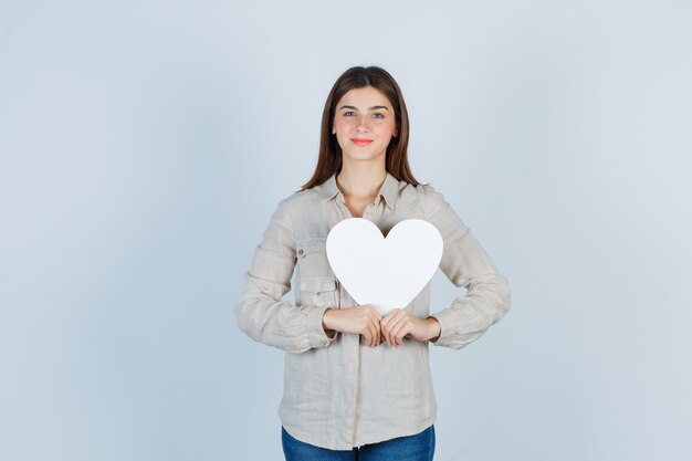 Ritratto di giovane bella femmina che tiene adesivo di carta in camicia e sembra allegra