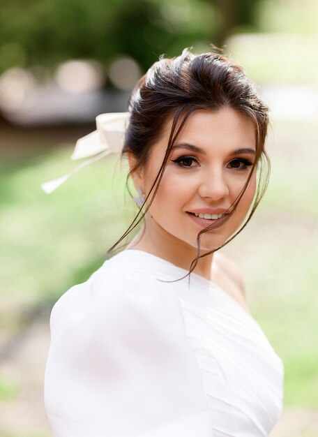 Ritratto di giovane bella ragazza con capelli castani legati, occhi castano scuro, compongono naturalmente un sorriso sincero e guardando la fotocamera mentre posano all'aperto