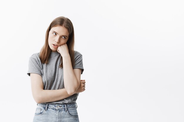 Ritratto di giovane bella ragazza infelice dello studente con capelli scuri in abbigliamento casual che osserva da parte con espressione stanca, tenendo la testa con la mano, essendo incazzato lezione noiosa.