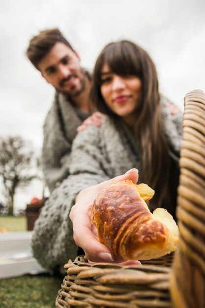 Ritratto di giovane coppia avvolto in coperta grigia dando croissant al forno