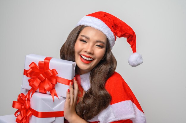 Ritratto di giovane donna abbastanza asiatica in costume rosso di babbo natale, sorridere e tenere in mano una scatola regalo