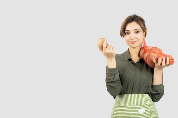 Ritratto di giovane donna adorabile dell'agricoltore che tiene le patate in borsa. Foto di alta qualità