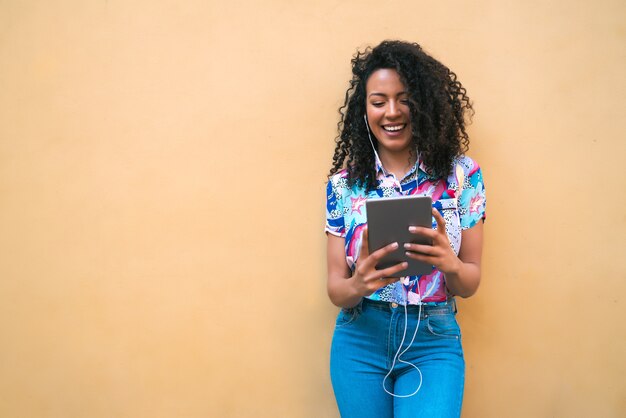 Ritratto di giovane donna afroamericana felice che ascolta musica sulla sua tavoletta digitale. Concetto di tecnologia.