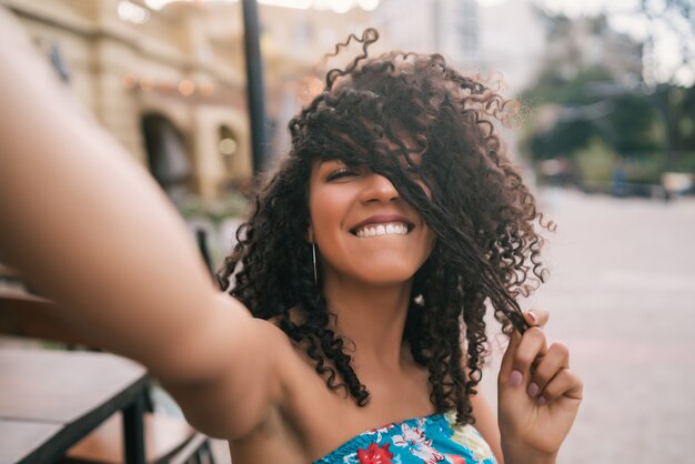 Ritratto di giovane donna afroamericana prendendo un selfie all'aperto in strada. Godersi la vita. Concetto di stile di vita.