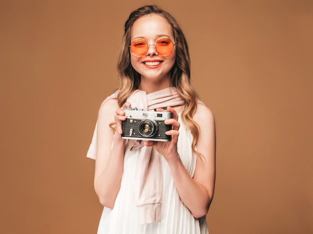 Ritratto di giovane donna allegra che prende foto con ispirazione e che porta vestito bianco. Ragazza che tiene la retro macchina fotografica. Posa di modello