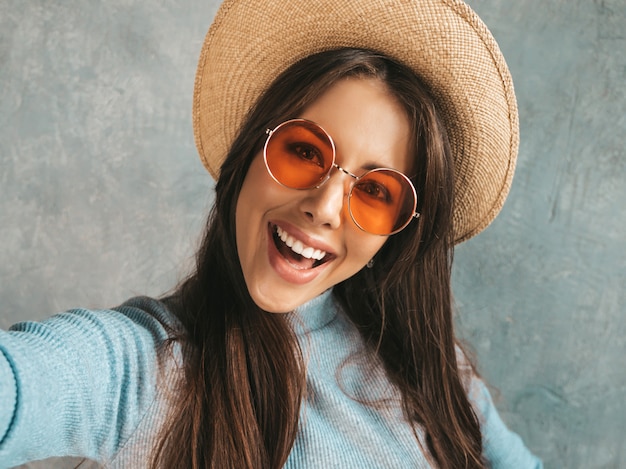 Ritratto di giovane donna allegra che prende il selfie della foto e che indossa vestiti e cappello moderni.