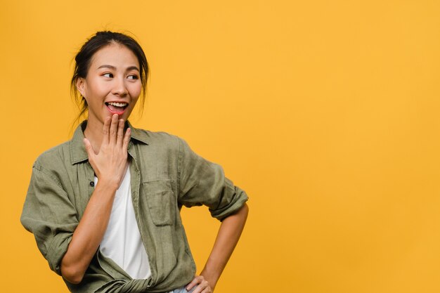 Ritratto di giovane donna asiatica con espressione positiva, sorriso ampiamente, vestito con abiti casual sul muro giallo. La donna felice adorabile felice si rallegra del successo. Concetto di espressione facciale.