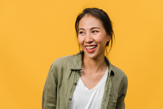 Ritratto di giovane donna asiatica con espressione positiva, sorriso ampiamente, vestito con abiti casual sul muro giallo. La donna felice adorabile felice si rallegra del successo. Concetto di espressione facciale.