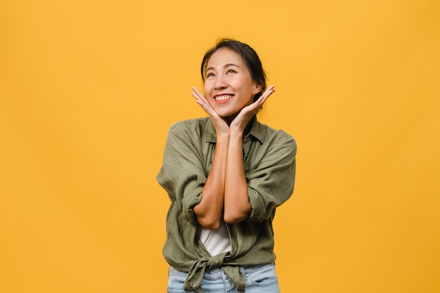 Ritratto di giovane donna asiatica con espressione positiva, sorriso ampiamente, vestito con abiti casual sul muro giallo. La donna felice adorabile felice si rallegra del successo. Concetto di espressione facciale.