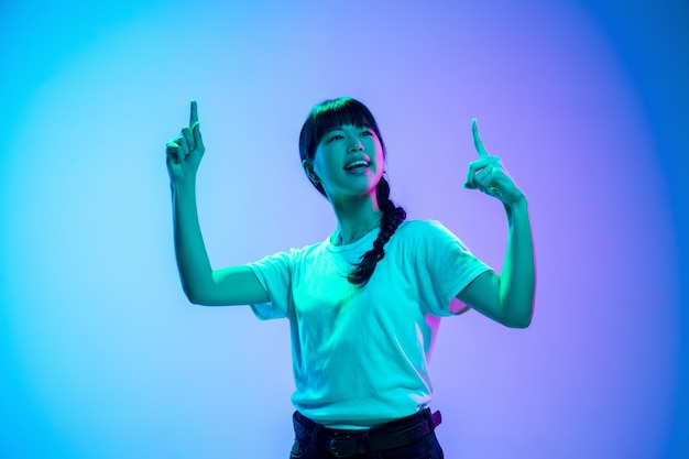 Ritratto di giovane donna asiatica su sfondo sfumato blu-viola studio in luce al neon. Concetto di gioventù, emozioni umane, espressione facciale, vendite, annuncio. Bellissima modella bruna.